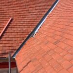 A roofer installing a red tiled roof on a house.