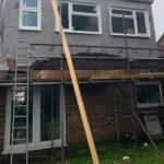 A house being re-roofed by a roofer with a ladder and scaffolding.